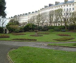 Shows a photograph of Adelaide Crescent. In the foreground is a circular garden display. The background shows a crescent of Regency houses.